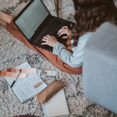Woman working on her laptop from home, surrounded by design elements on the floor.