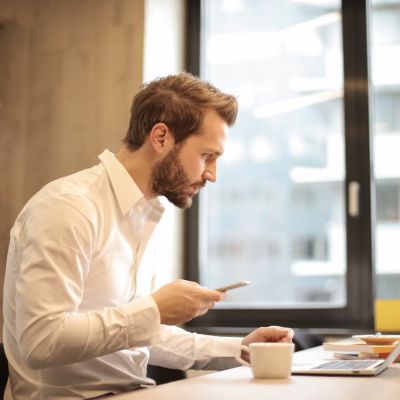 Focused businessman working on laptop while checking smartphone in modern office.